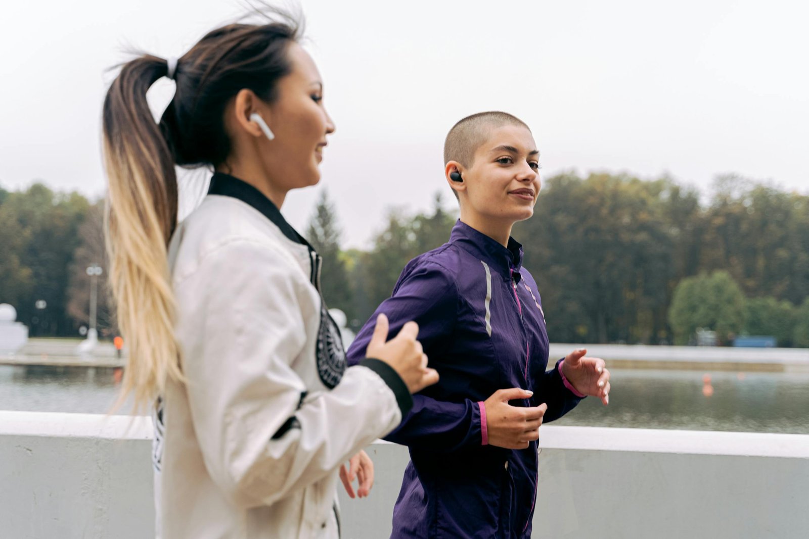 Two women jogging outdoors near a lake in sportswear, promoting a healthy lifestyle.