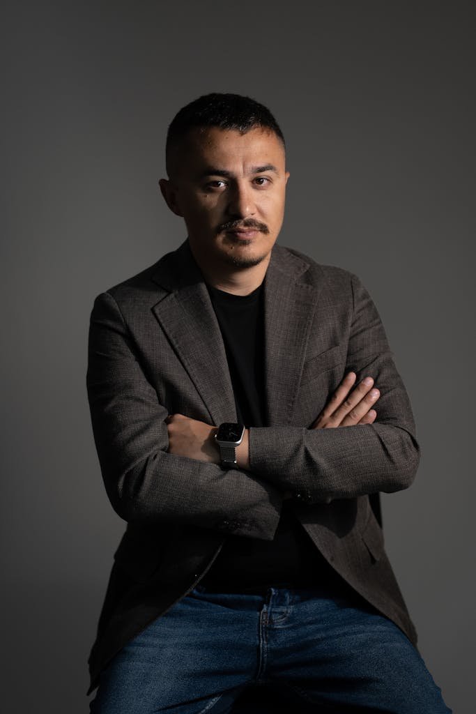 A confident man in business casual attire poses in a studio environment, arms crossed.