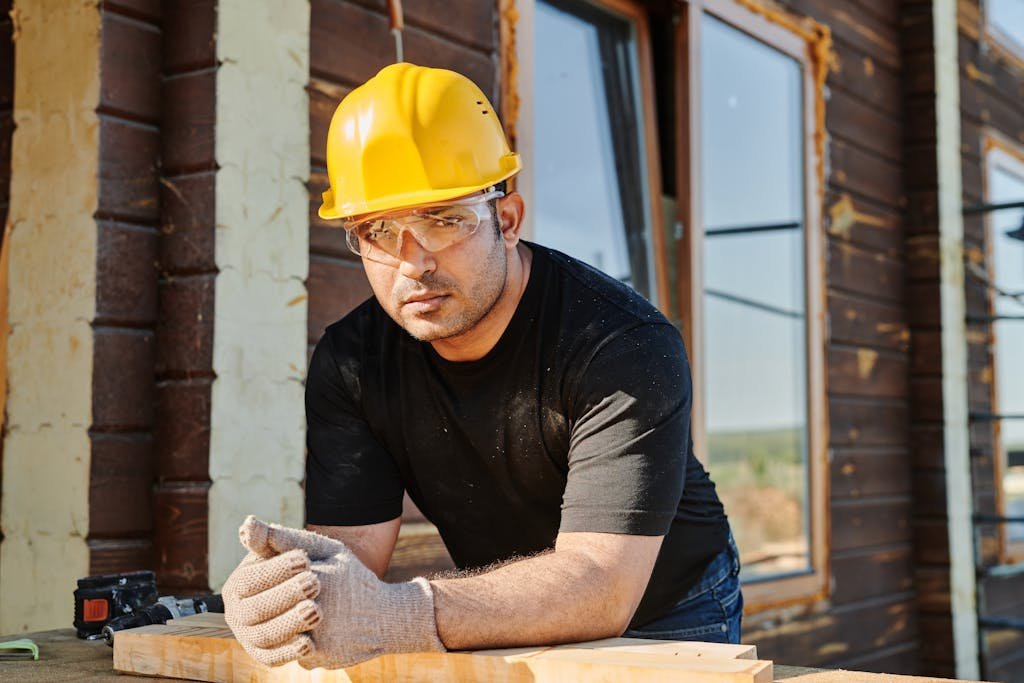 Focused construction worker with safety gear at a woodwork site.