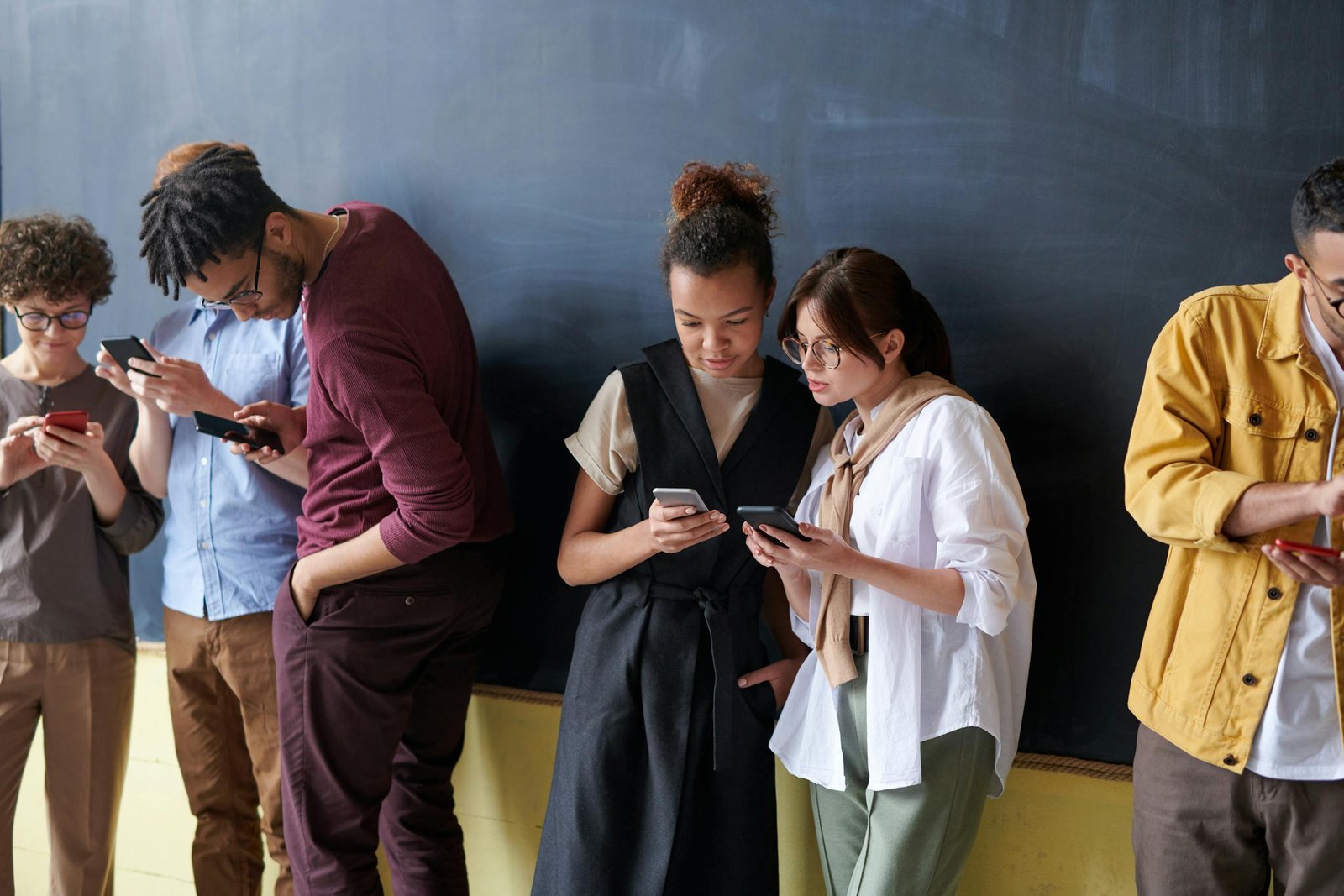 A diverse group of young adults using smartphones in a casual indoor setting.