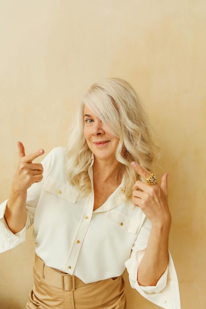Elegant senior woman with white hair smiling and posing confidently against a neutral background.